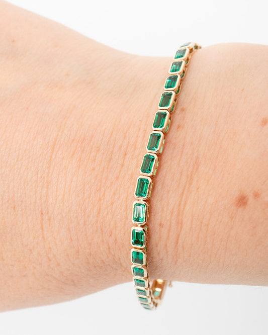 Gold bracelet with green gemstones on a wrist against a white background