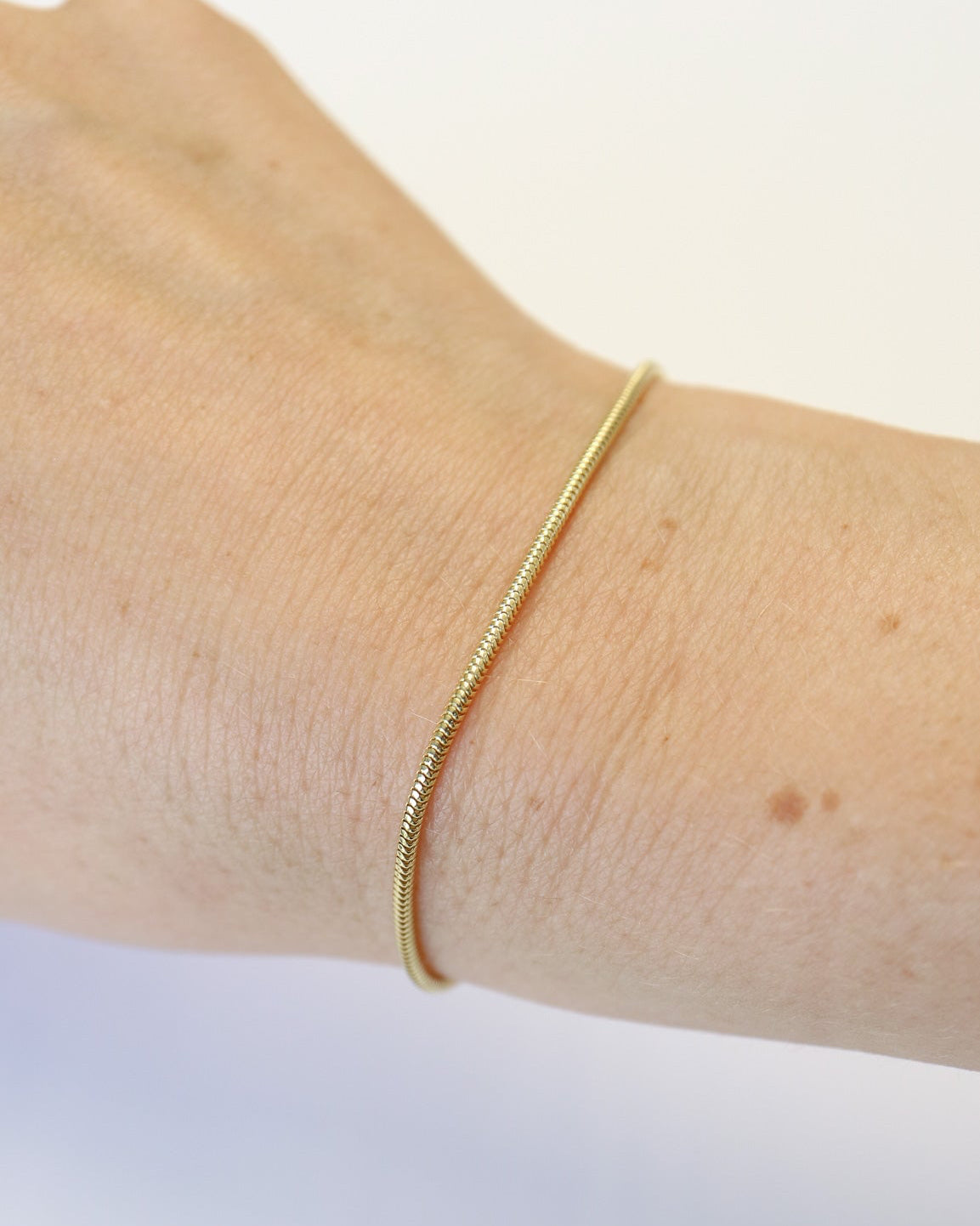 9ct solid gold skinny snake chain necklace with a delicate, flexible design and polished gold finish, photographed on an off-white background.