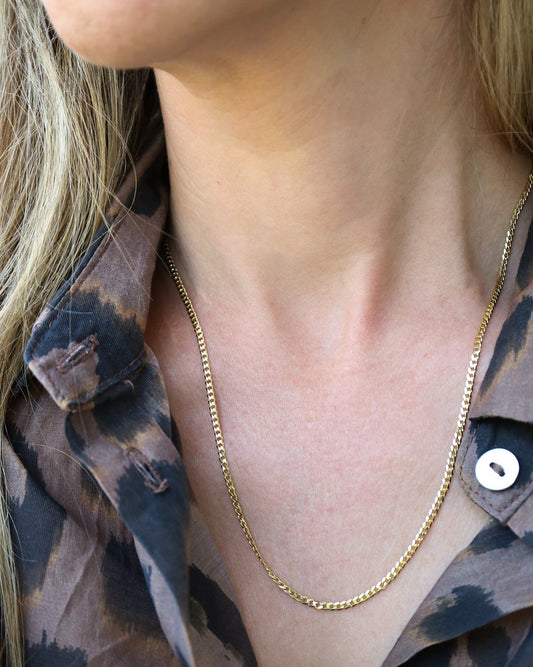 9kt solid gold Flat Curb Chain necklace featuring polished, flattened interlocking links, photographed on a female neck
