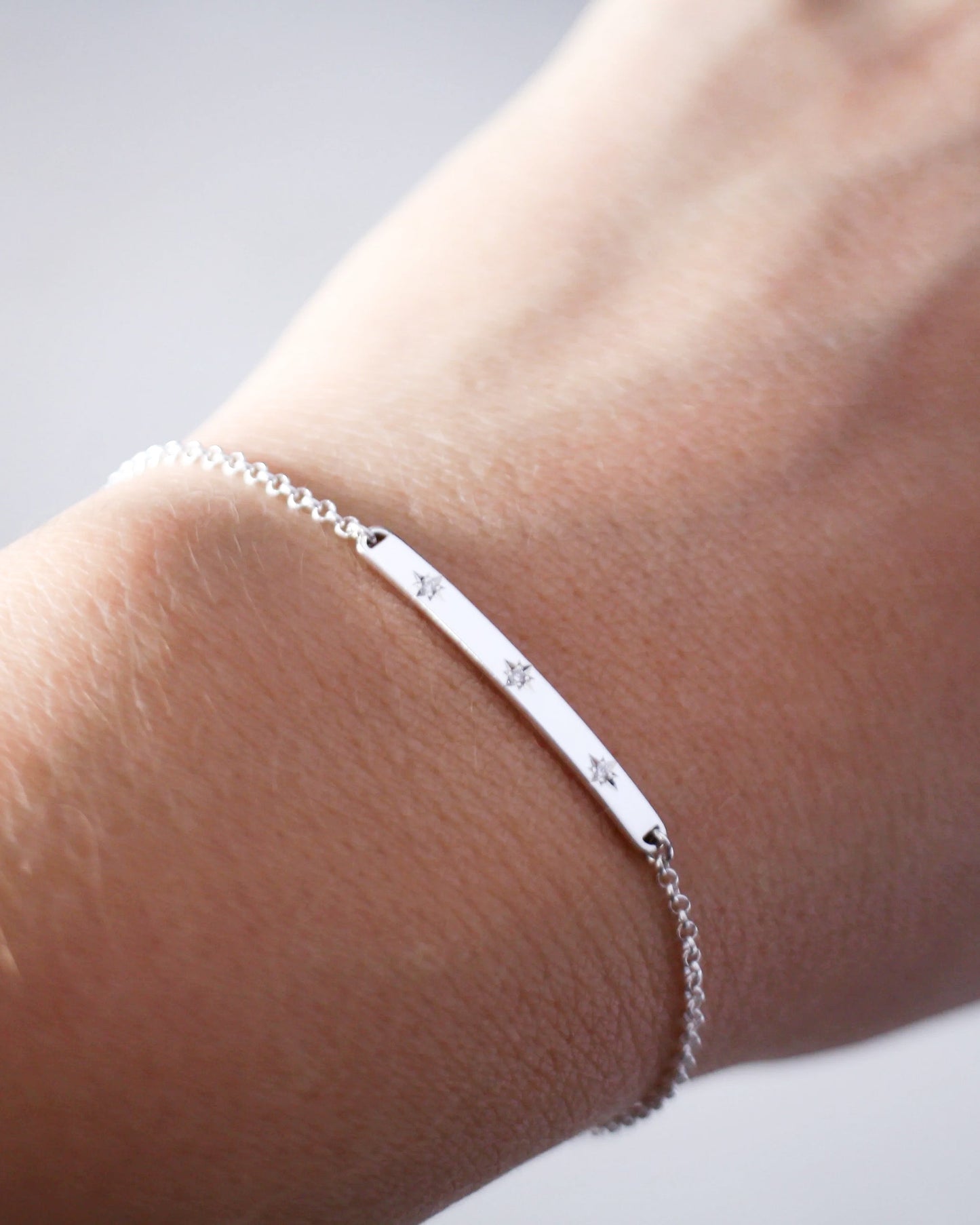 Silver bracelet with engraved stars on a wrist against a neutral background