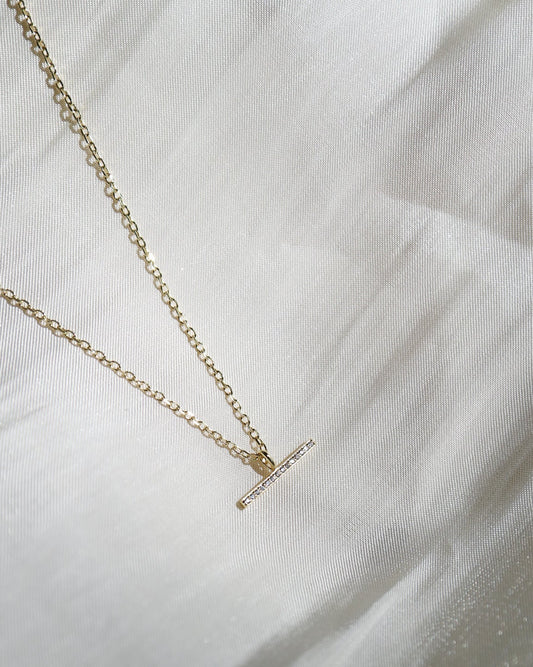 Gold necklace with a small pendant on a white fabric background