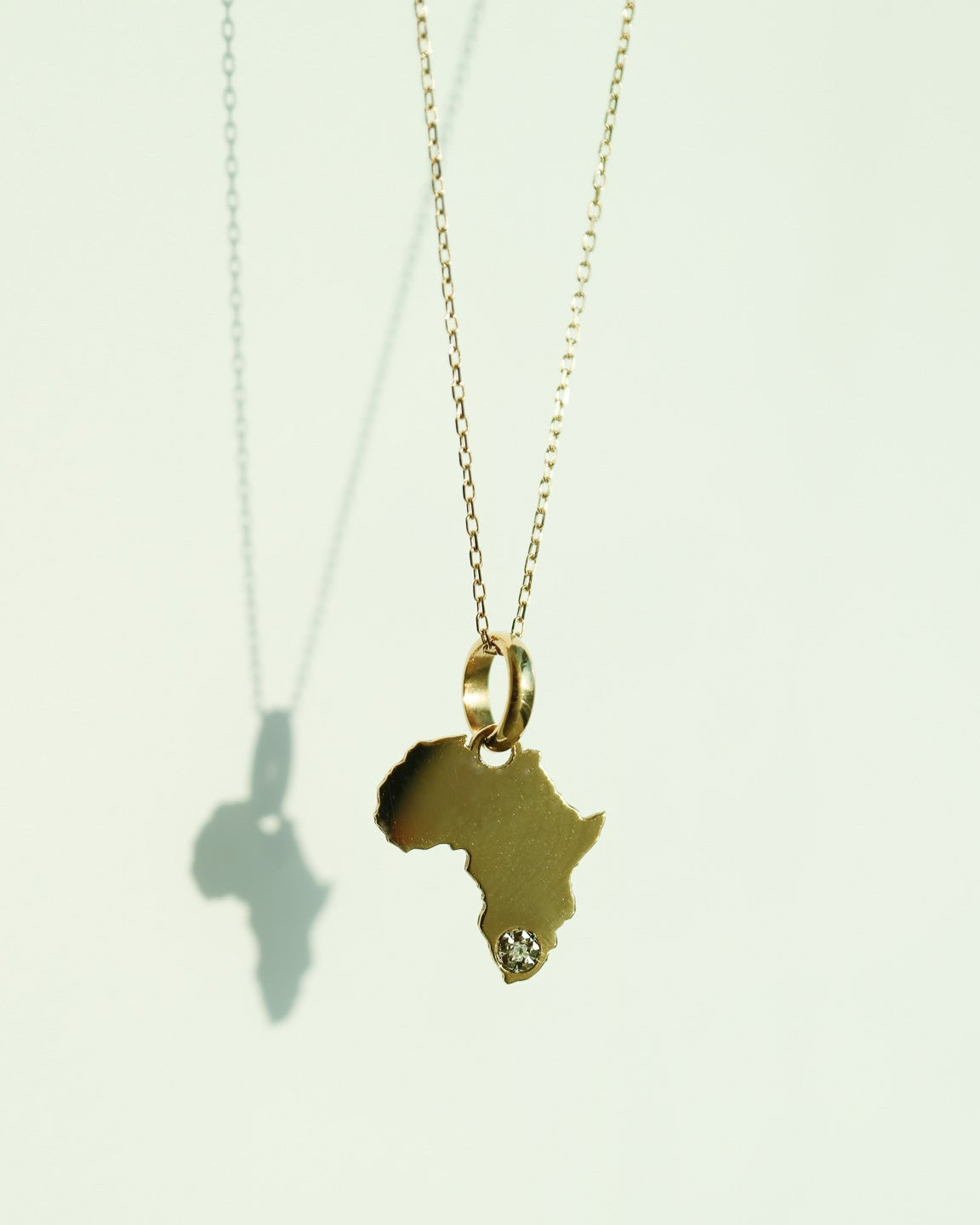9ct Gold necklace with an Africa-shaped pendant with natural diamond on a light gray background