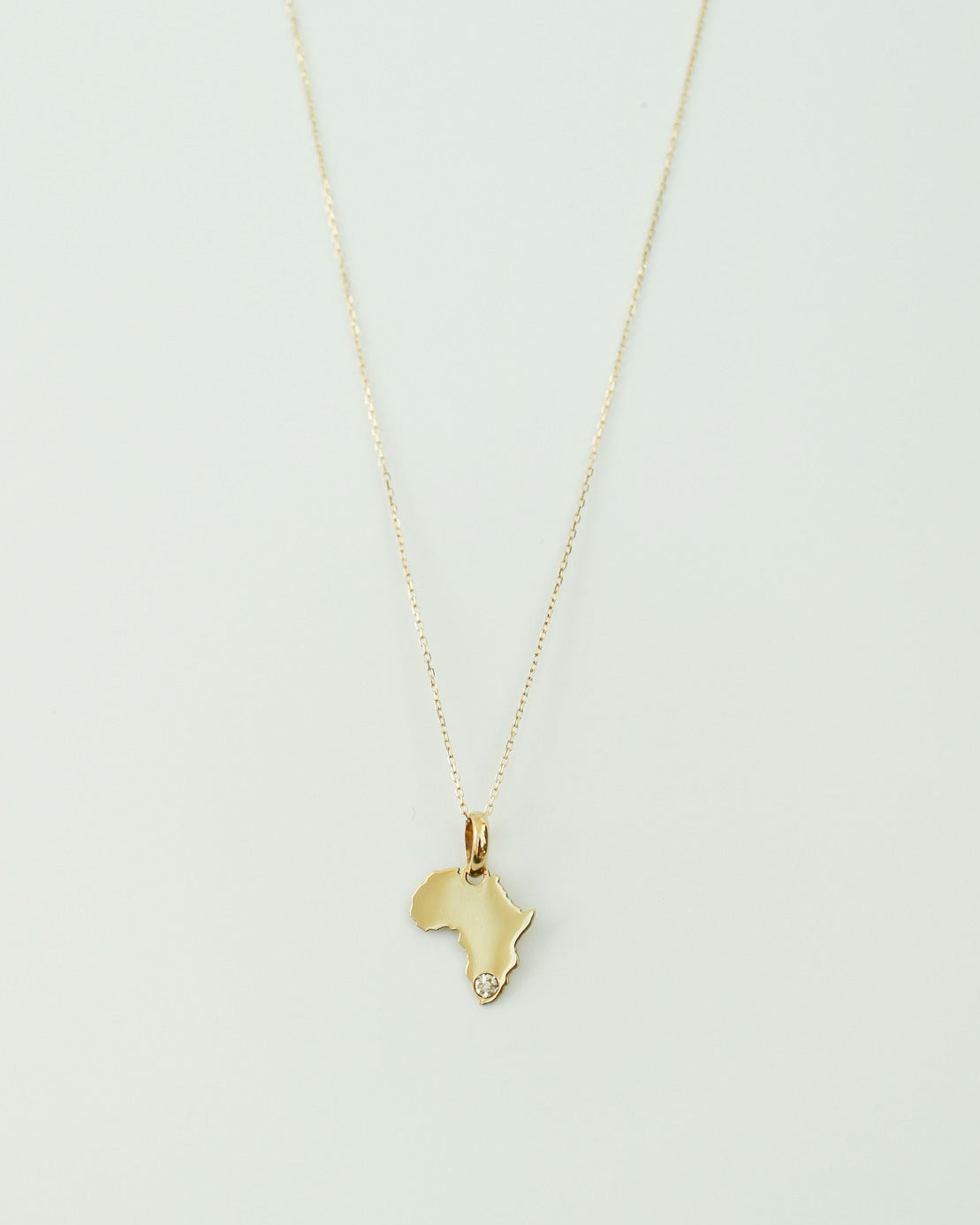 9ct Gold necklace with an Africa-shaped pendant with natural diamond on a light gray background