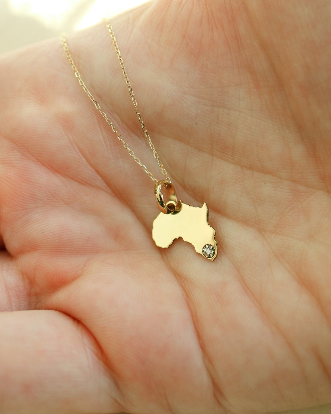 Gold necklace with a small pendant shaped like Australia held in a hand.