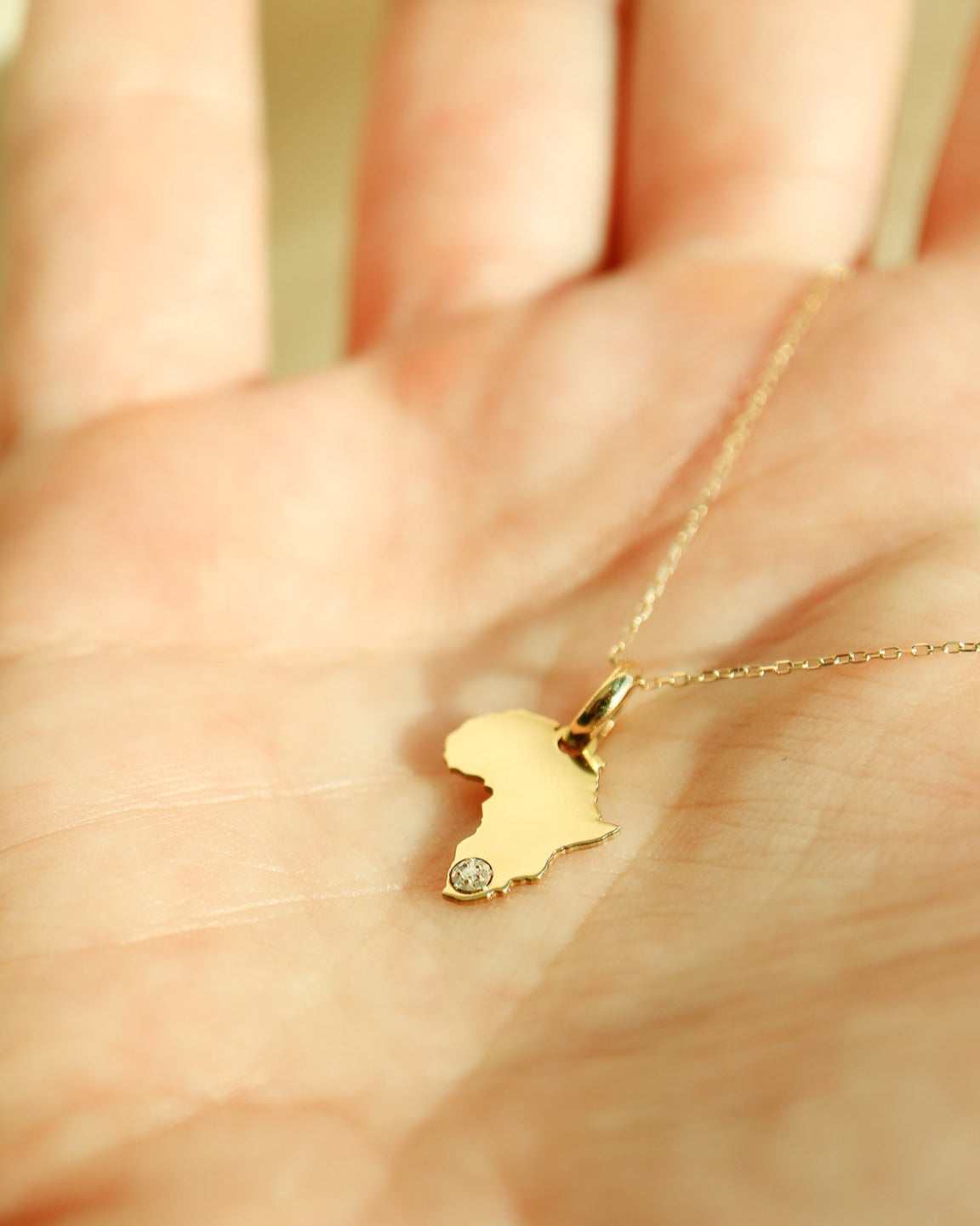 Gold necklace with a pendant shaped like Africa held in a hand.