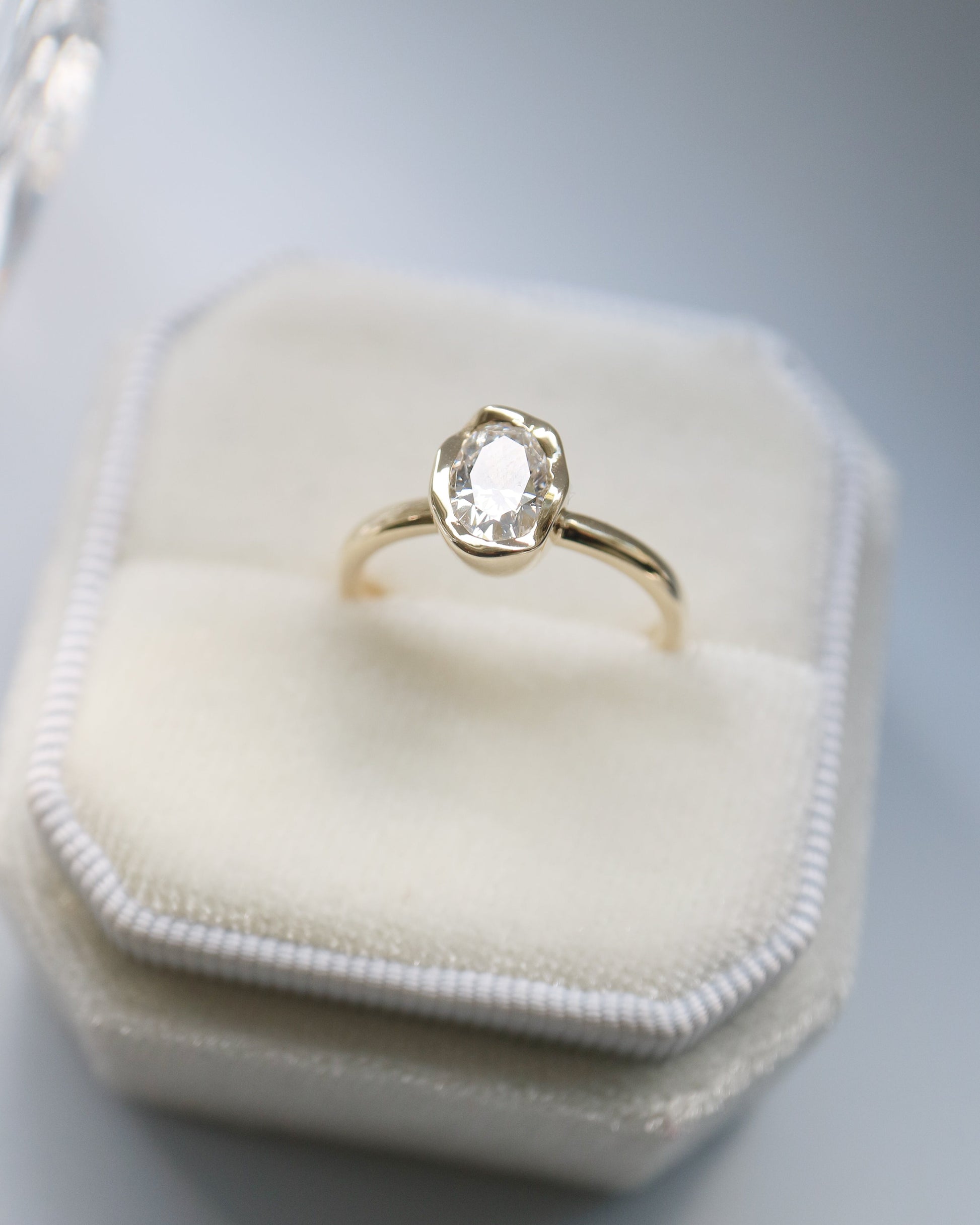 Gold ring with a diamond on a white hexagonal jewelry box against a gray background