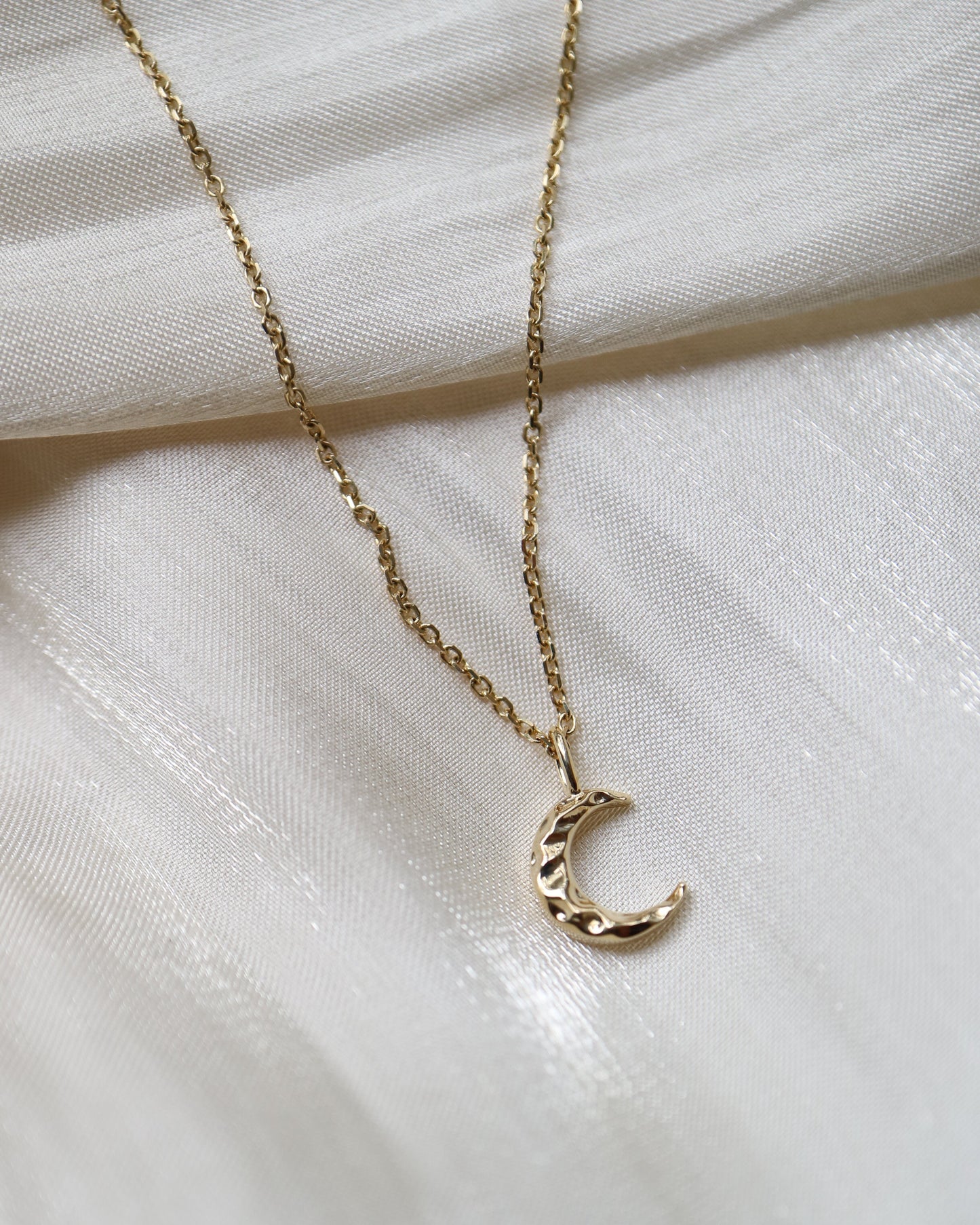 Gold necklace with a crescent moon pendant on a white fabric background