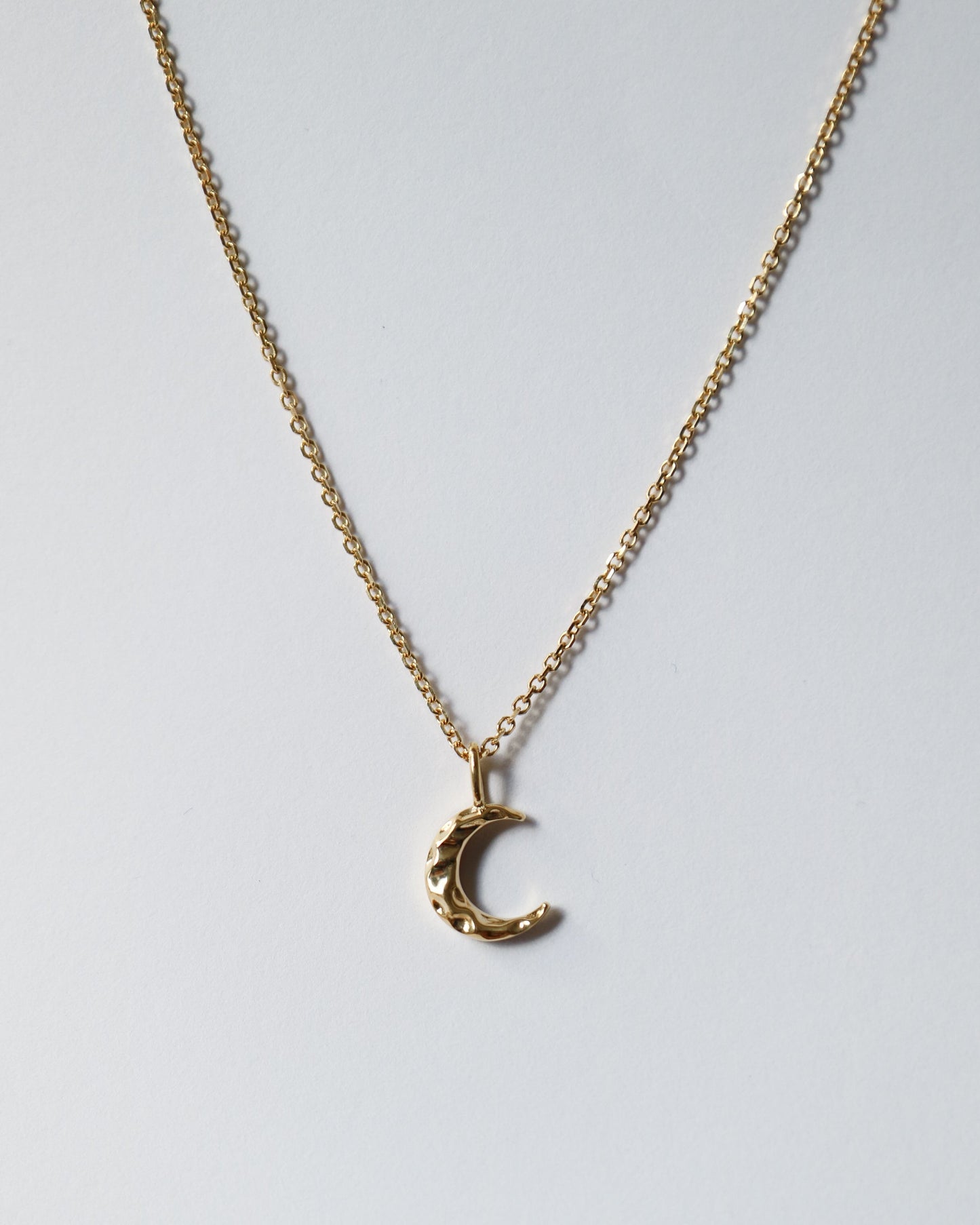 Gold crescent moon necklace on a light gray background