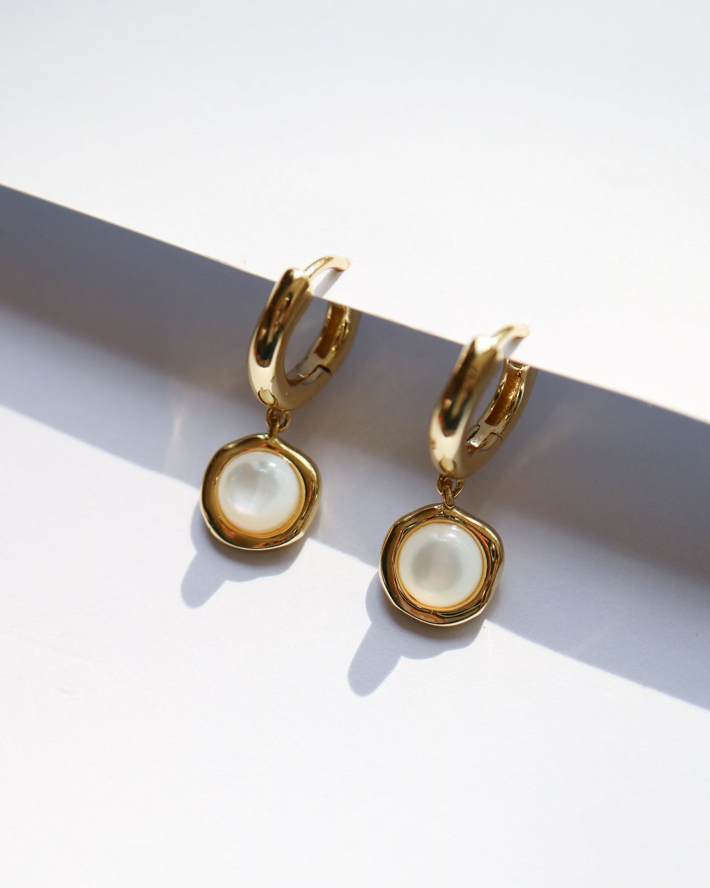 Gold hoop earrings with pearl-like centers on a white background