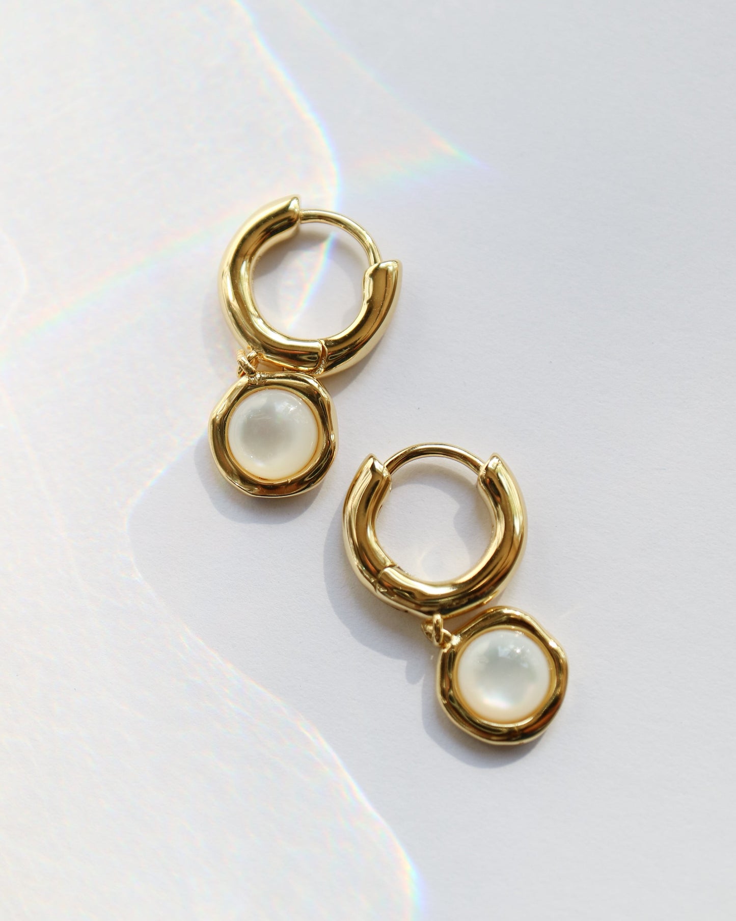 Gold hoop earrings with pearl-like stones on a white background