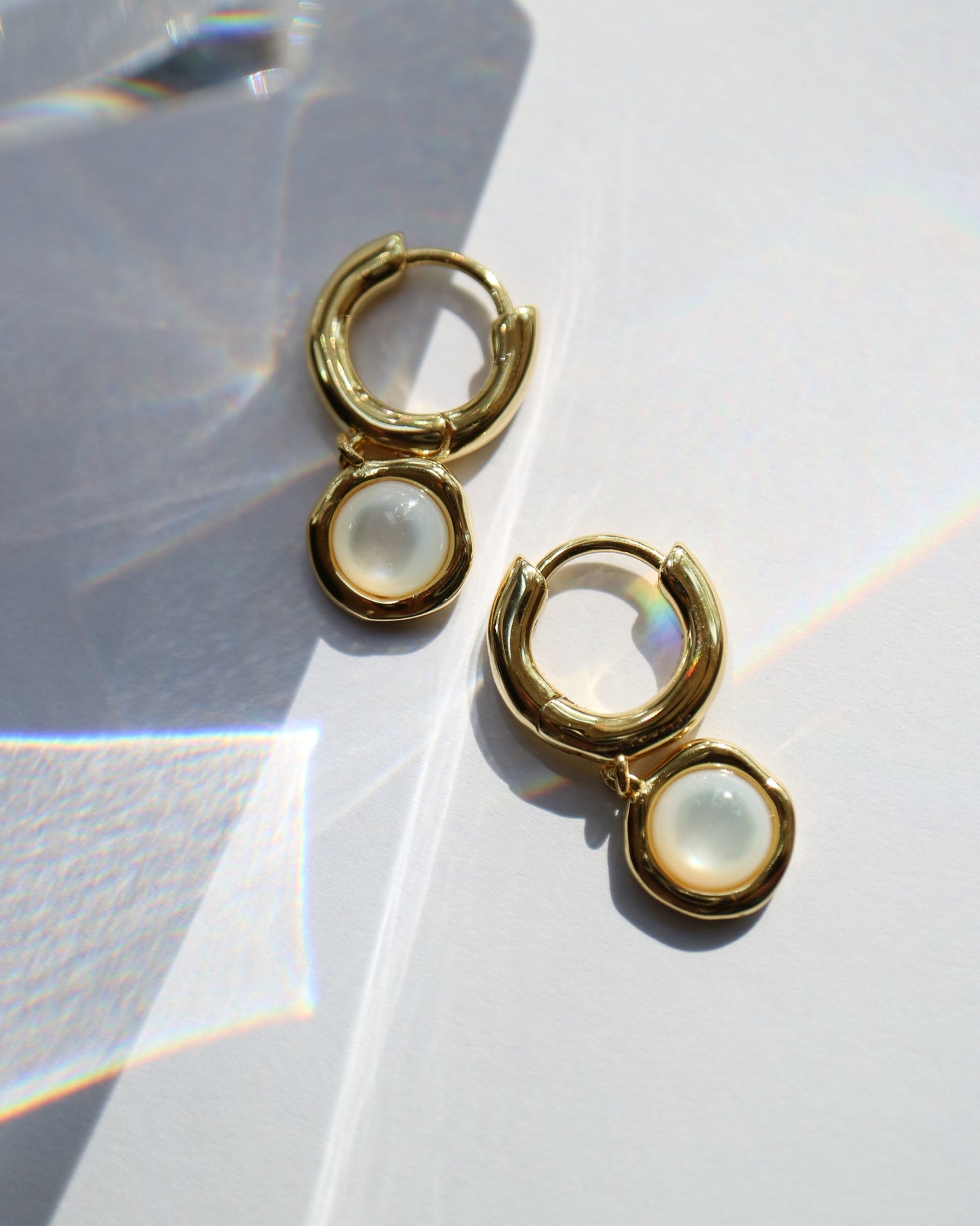 Gold hoop earrings with a central gemstone on a light background