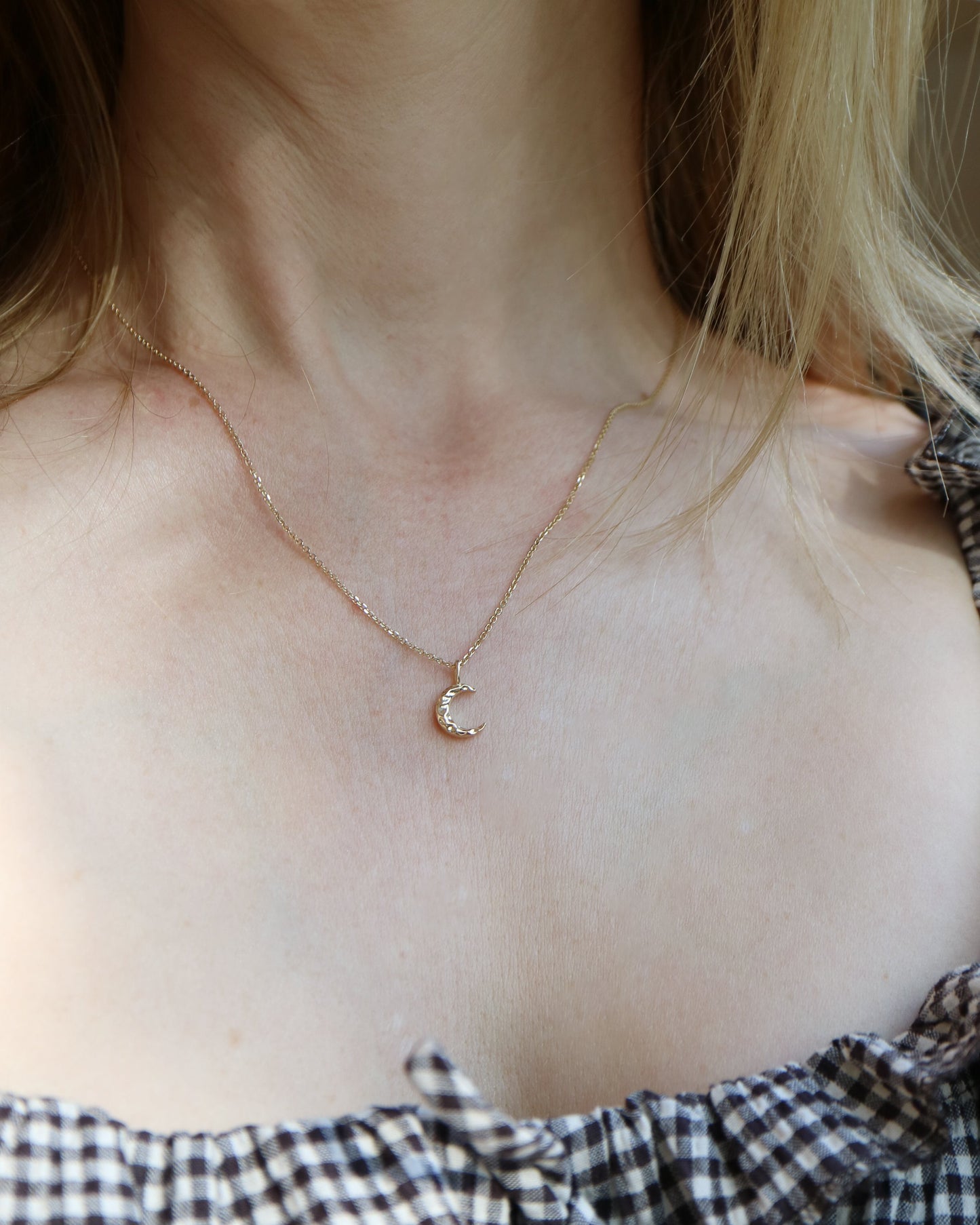 Necklace with a small round pendant worn by a person with checkered clothing.