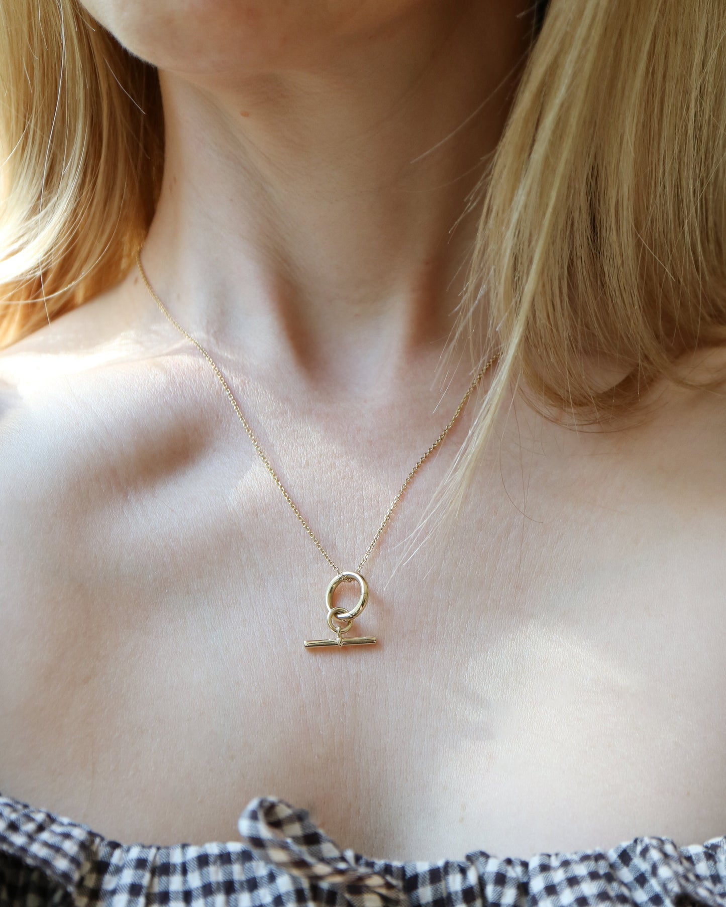 Necklace with a small pendant worn by a person in a checkered top.