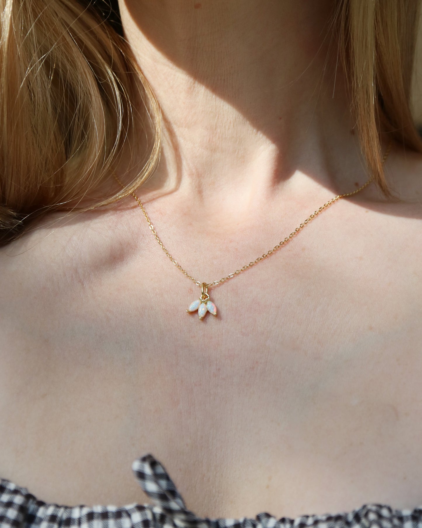 Necklace with a small pendant worn by a person with blonde hair, wearing a black and white checkered top.