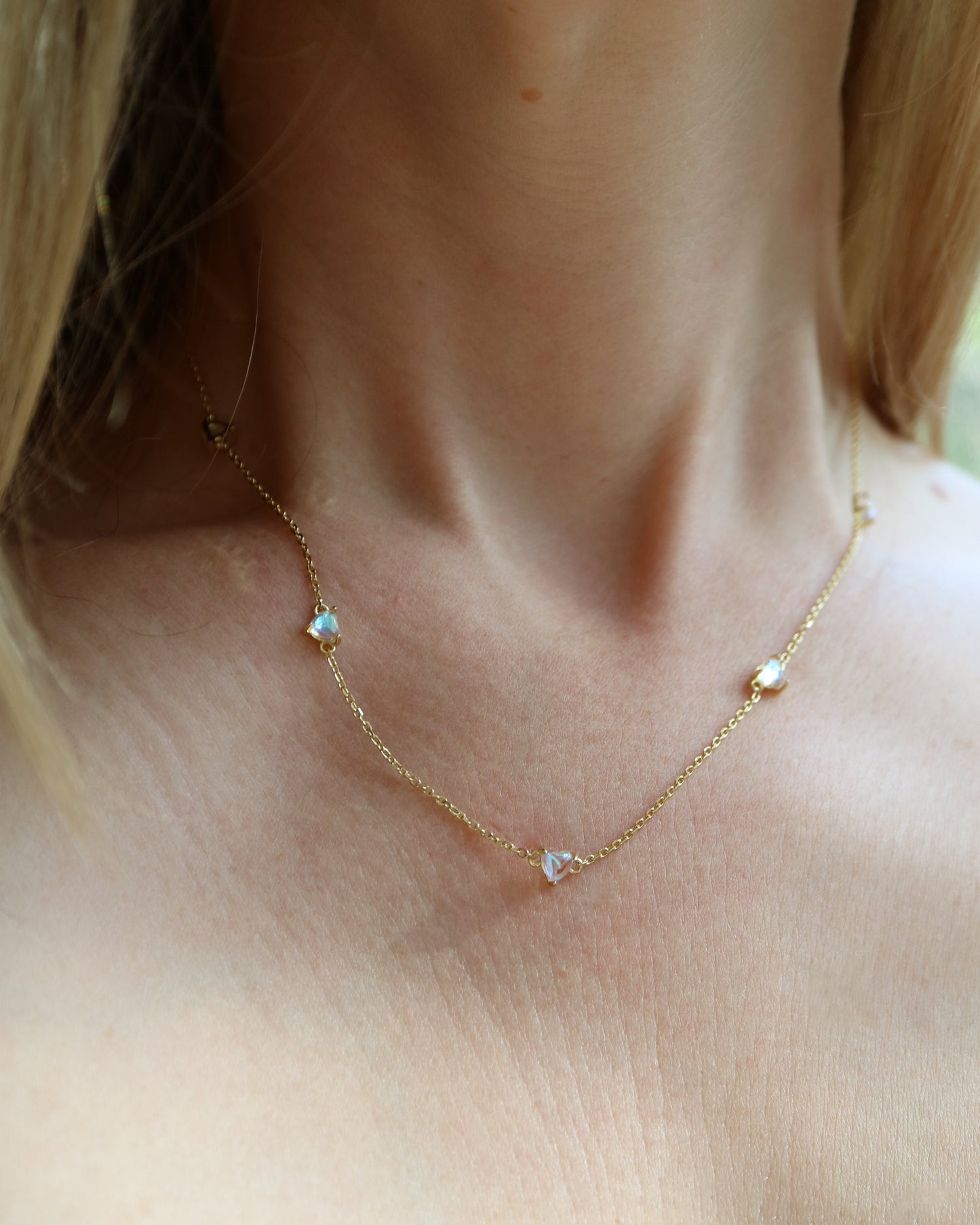 Close-up of a gold necklace with small heart-shaped pendants on a person wearing a checkered top.