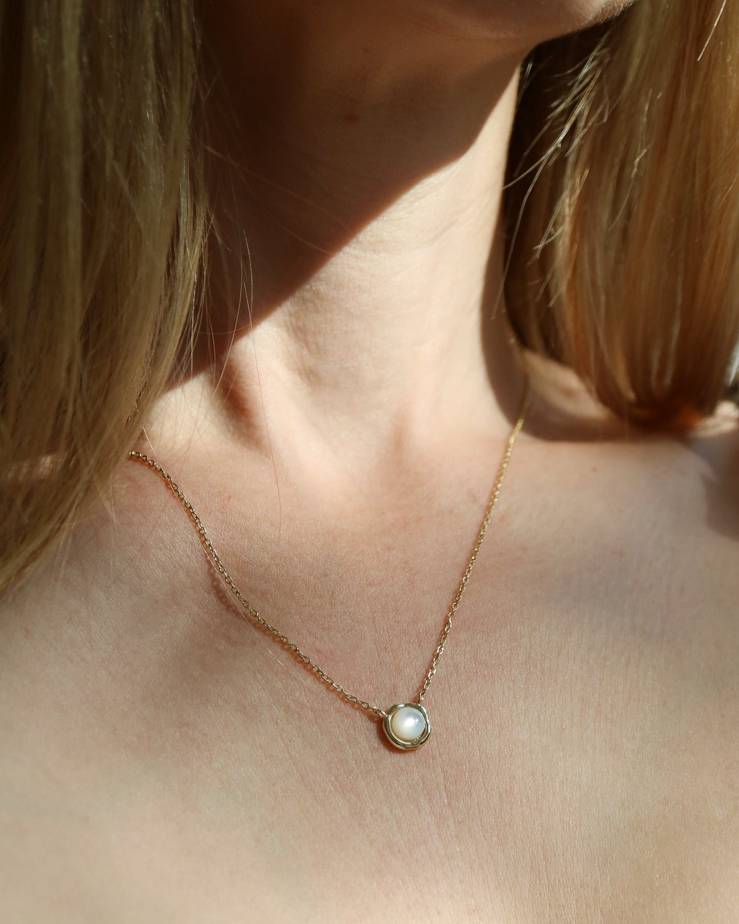 Necklace with a pendant worn by a person with shoulder-length hair.