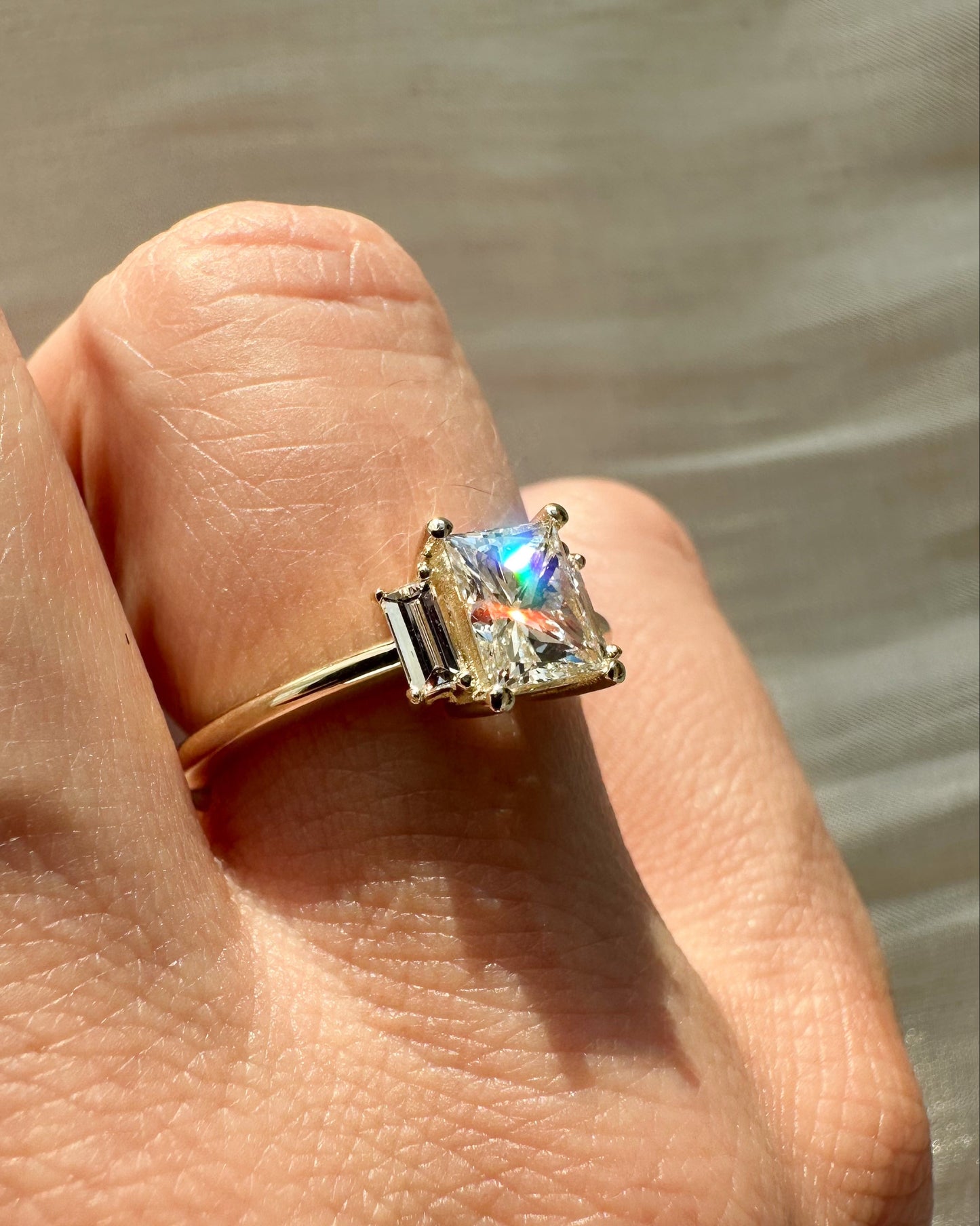 Gold ring with a colorful gemstone on a finger against a neutral background