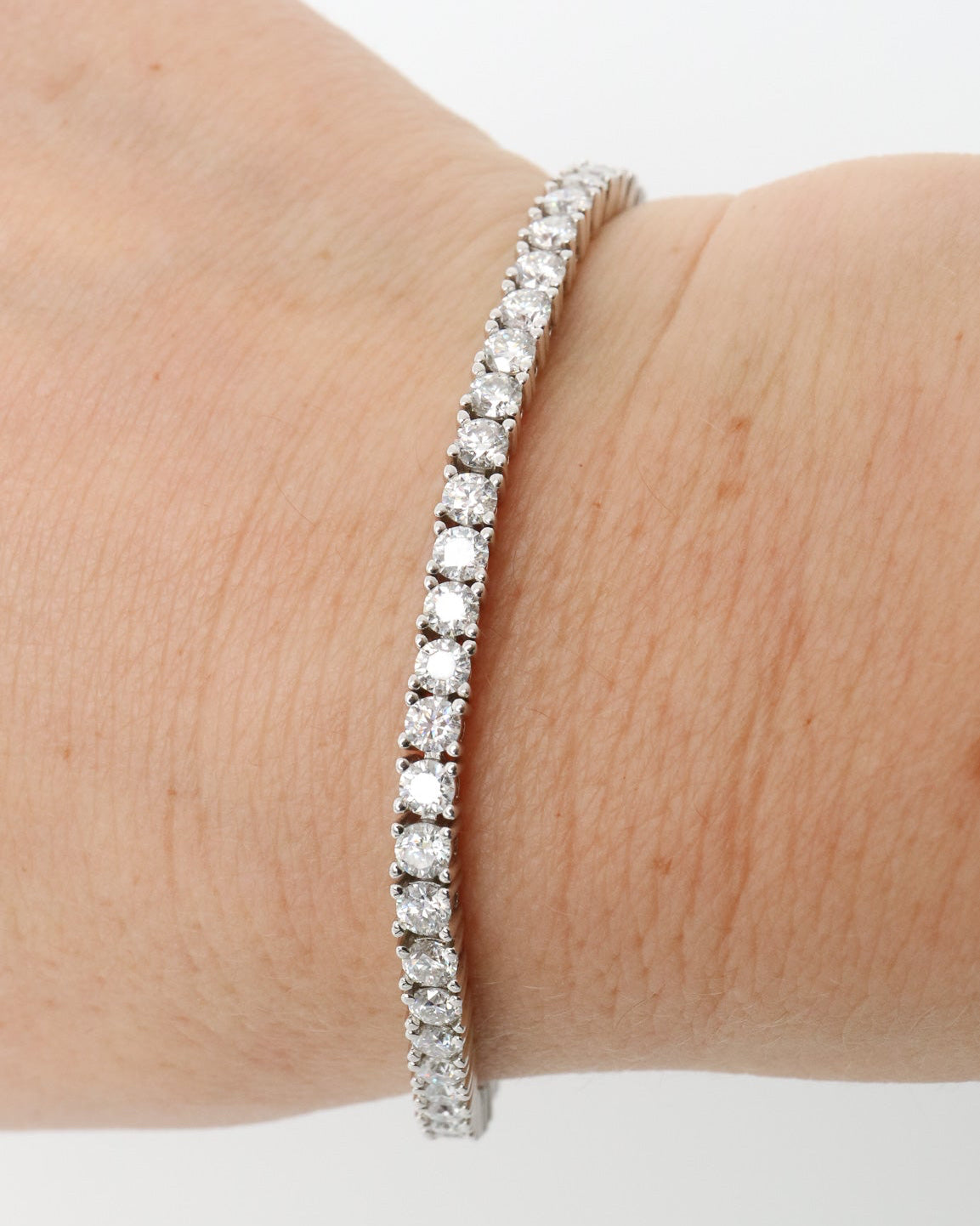 A silver tennis bracelet with a continuous line of clear round-cut stones, shown worn on a person's wrist against a plain white background.
