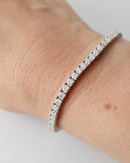 A silver tennis bracelet with sparkling clear stones worn on a person's wrist against a plain light background.