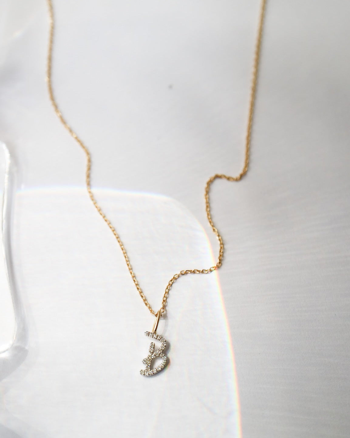 A delicate gold chain necklace with a small, silver-toned pendant adorned with tiny clear stones, displayed on a white textured surface.