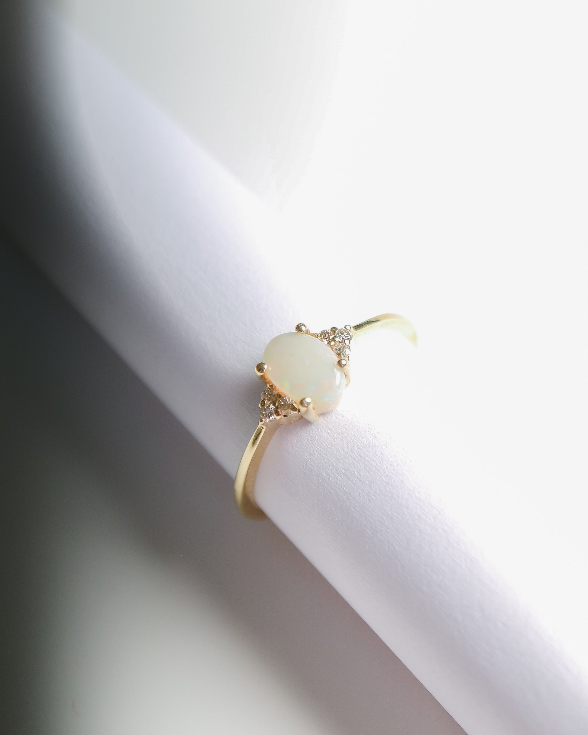 A 9kt gold ring featuring an oval opal cabochon center stone with natural white diamonds on either side, set on a thin gold band.