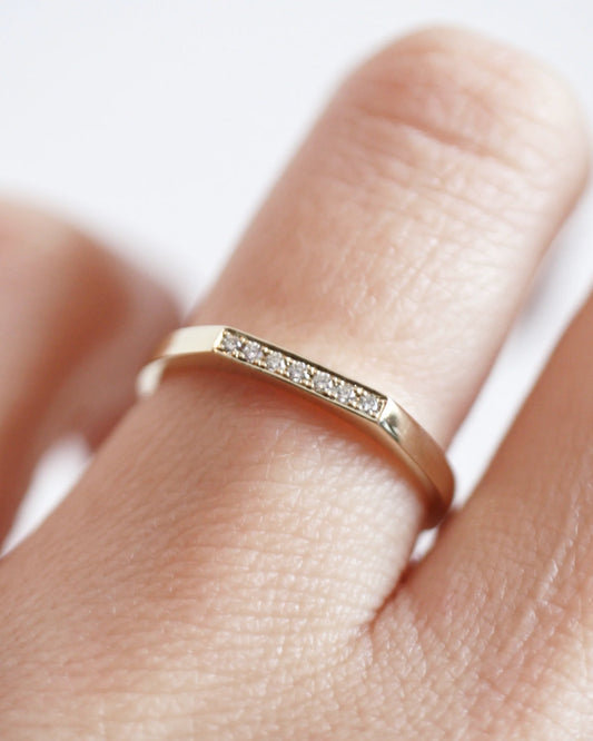 Gold ring with small diamonds on a finger against a white background
