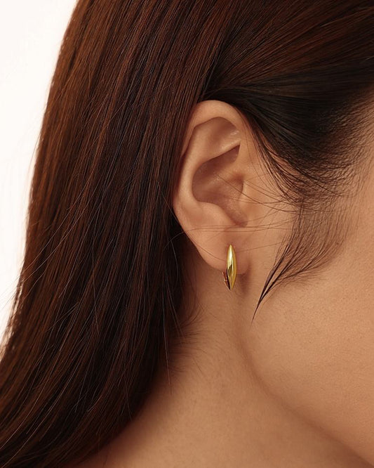 Close-up of a person wearing a gold hoop earring with a neutral background