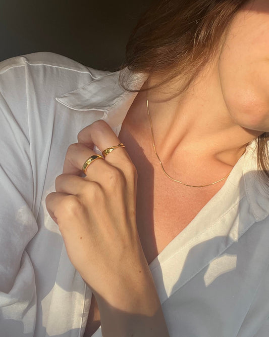 Person wearing a gold ring and gold necklace with a soft focus background
