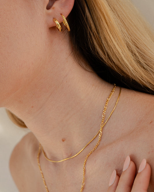 Close-up of a person wearing gold jewelry including earrings, necklace, and ring.