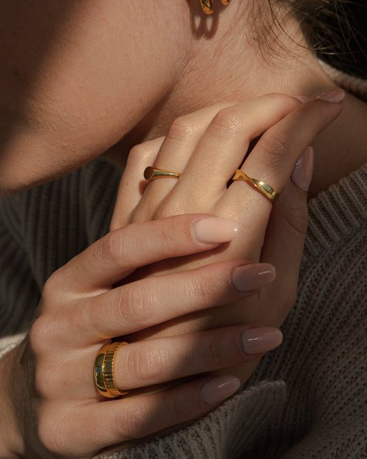 Close-up of a person wearing gold hoop earrings and rings on a neutral background