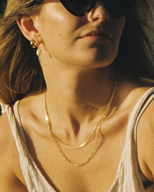 Close-up of a woman wearing sunglasses and a beige tank top with a gold necklace.