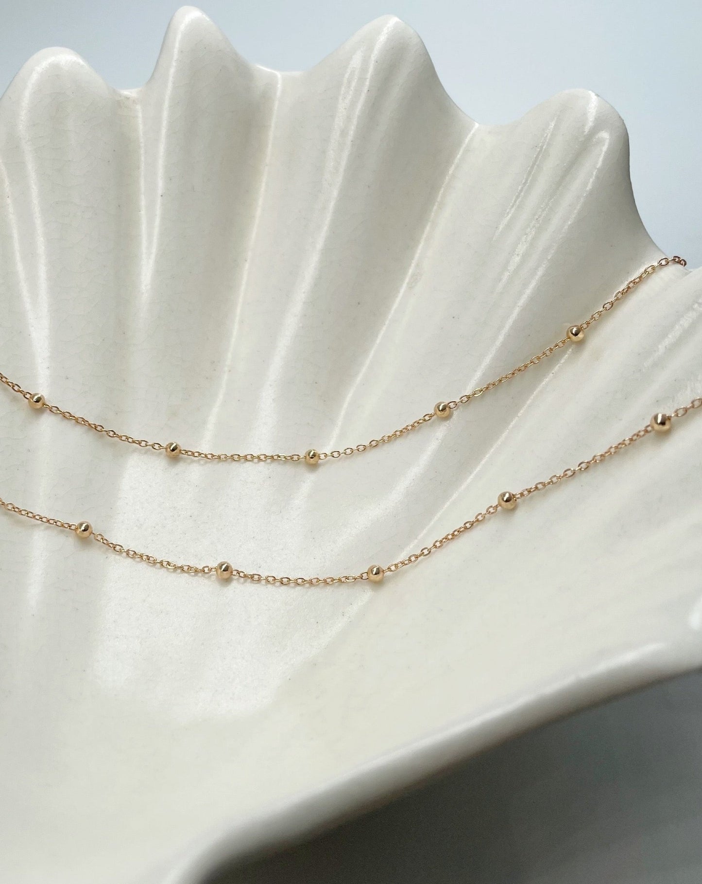 9k gold beaded chain draped over ceramic shell bowl