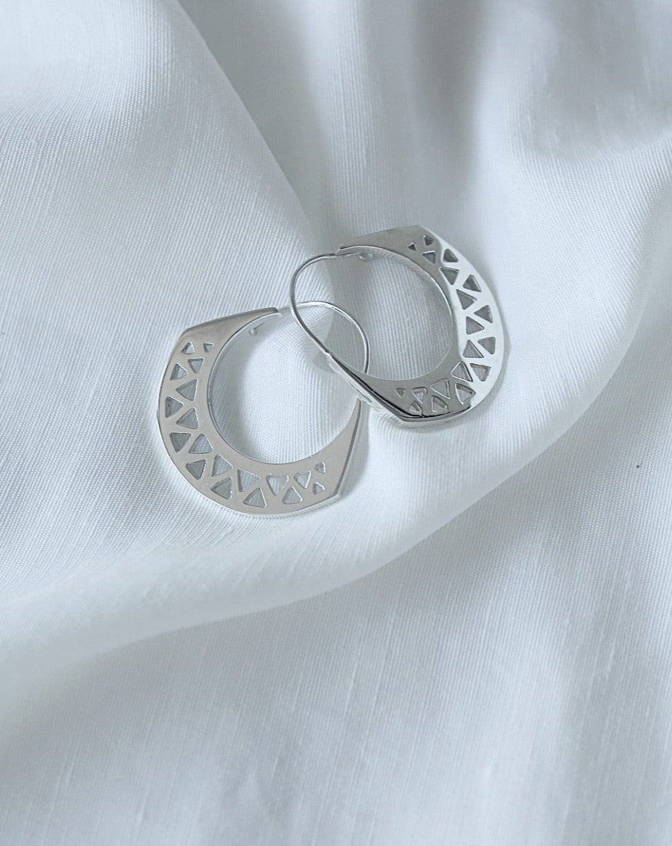 Sterling silver statement earrings with triangle cutouts on white linen background