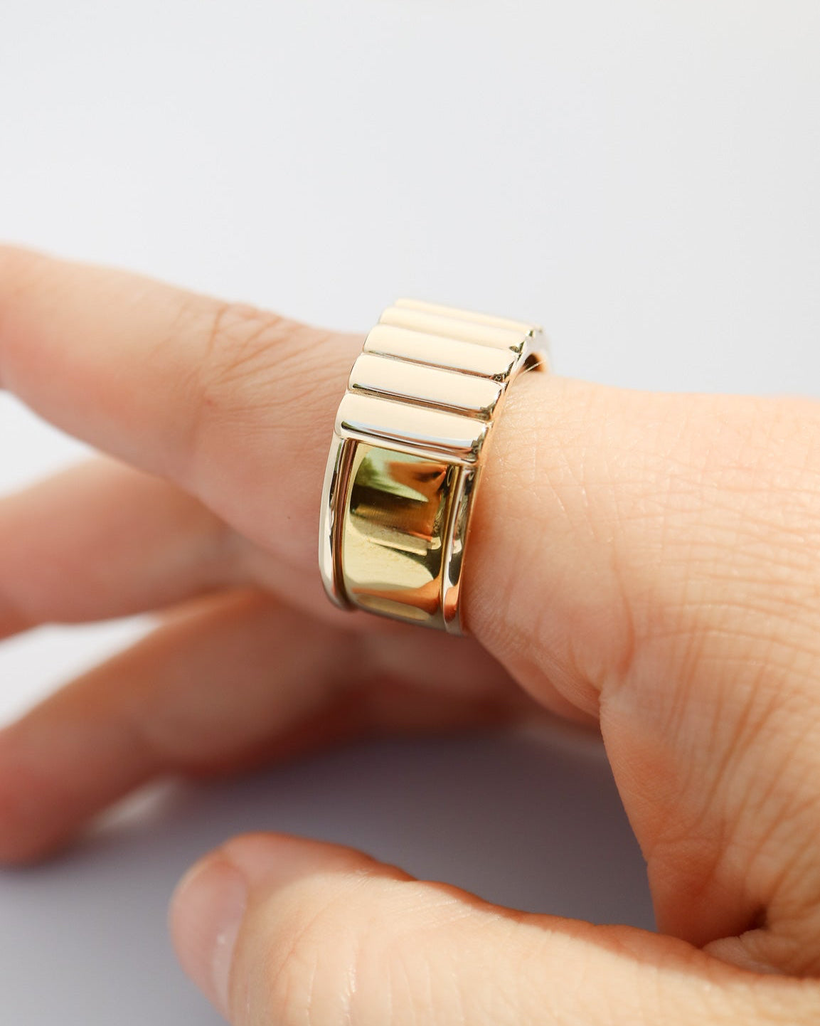 A close-up of a hand wearing a wide, chunky gold Oura ring jacket with a segmented, geometric design.