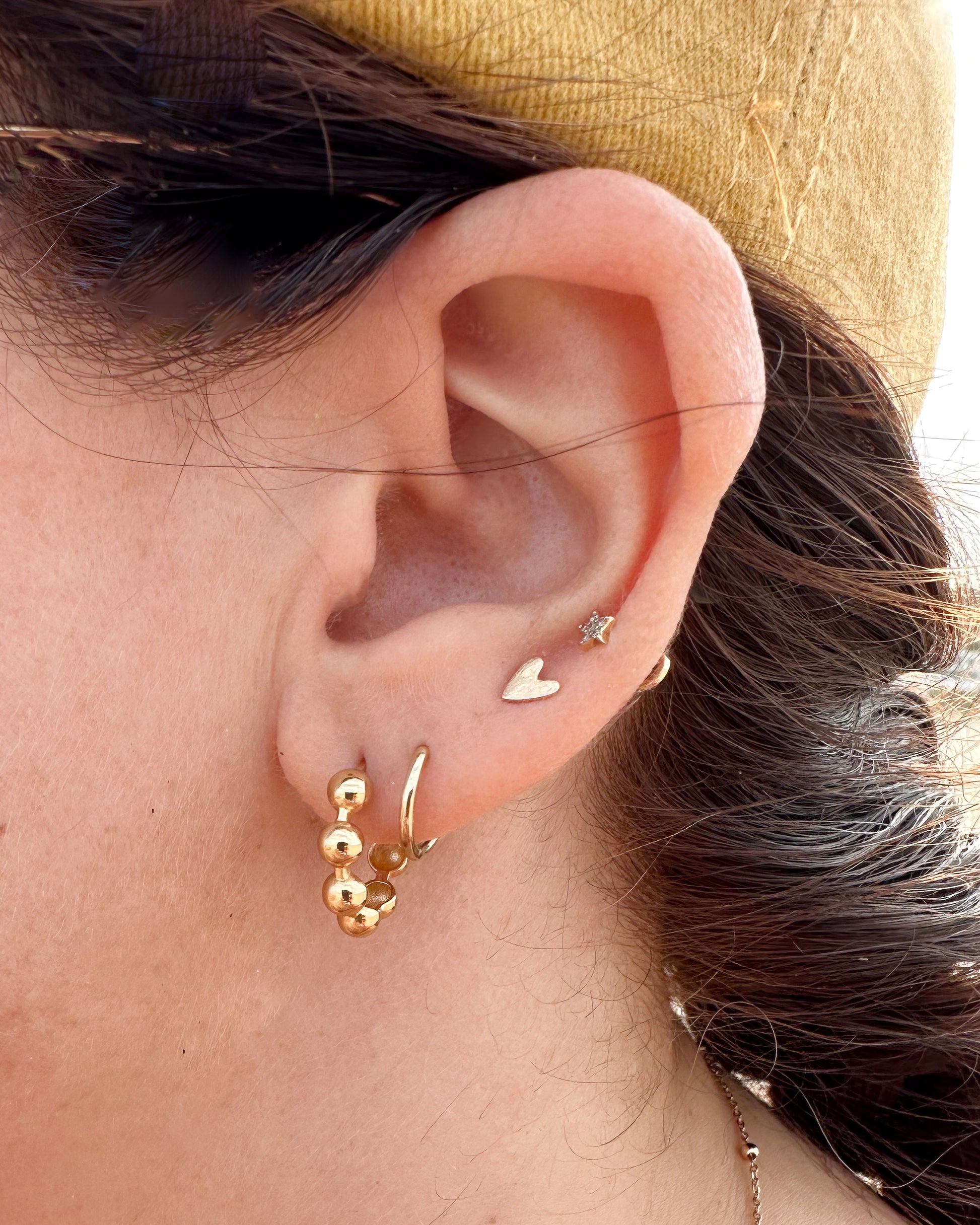 Close-up of an ear with gold earrings against a neutral background