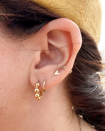 Close-up of an ear with gold earrings against a neutral background