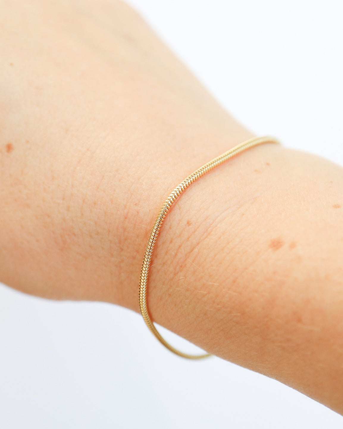 9ct solid gold skinny snake chain bracelet on a female wrist with a delicate, flexible design and polished gold finish, photographed on an off-white background.