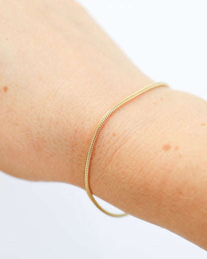 9ct solid gold skinny snake chain bracelet on a female wrist with a delicate, flexible design and polished gold finish, photographed on an off-white background.
