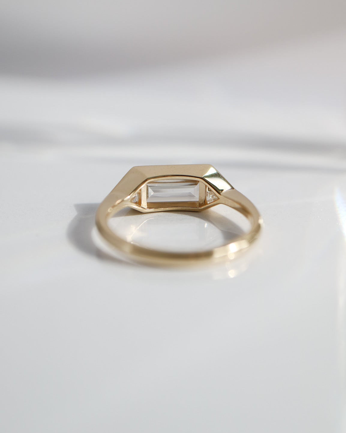 Gold ring with a rectangular gemstone on a light gray background