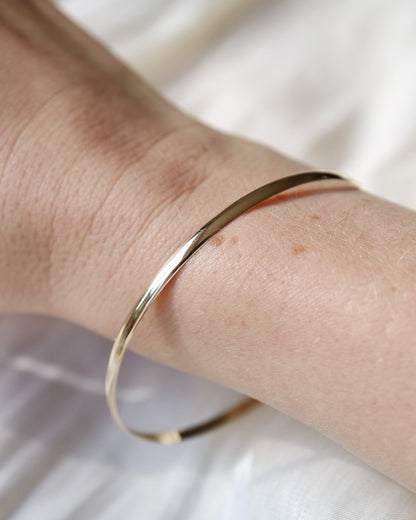 Gold bracelet on a wrist with a soft white background