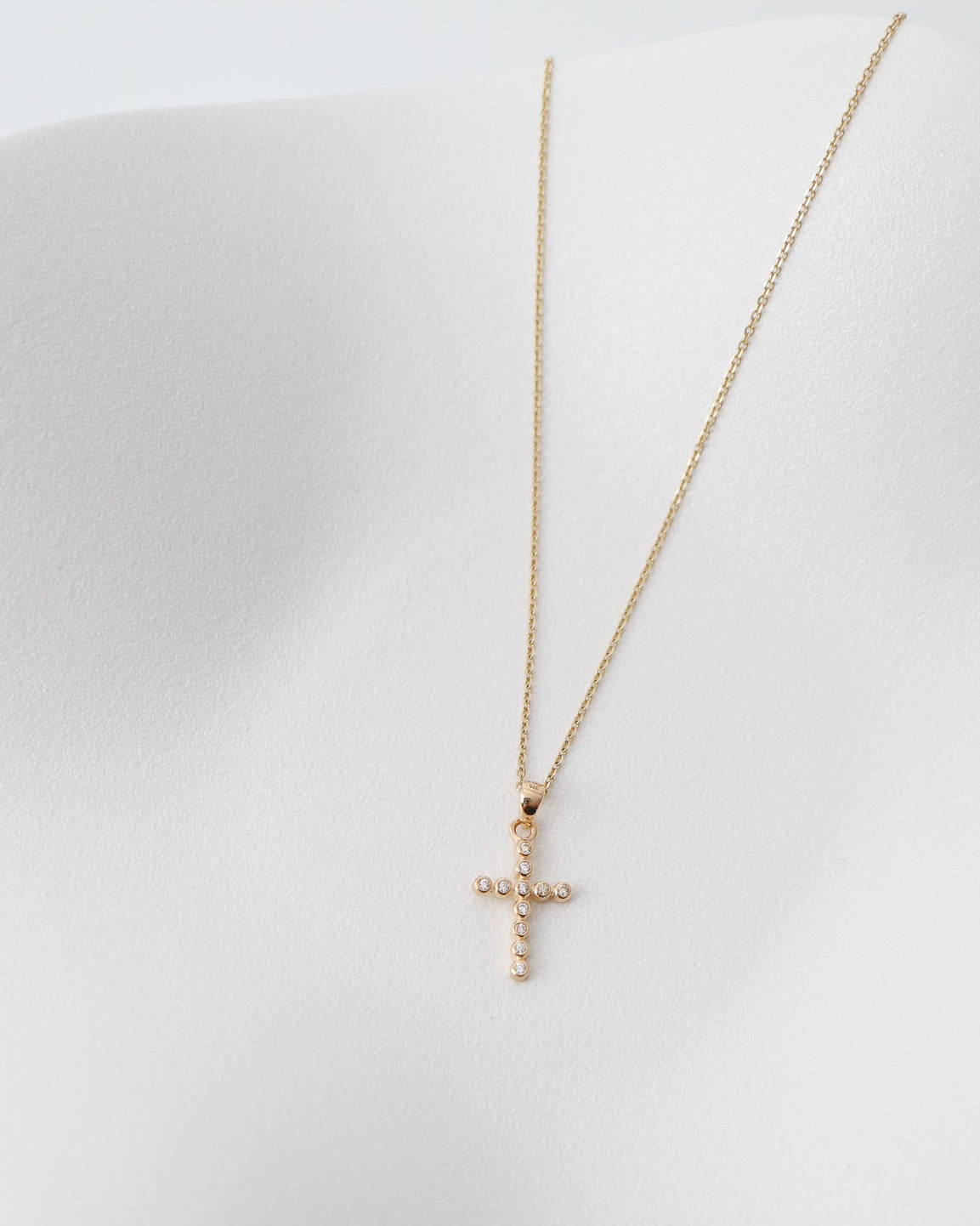 Gold necklace with a cross pendant on a white surface