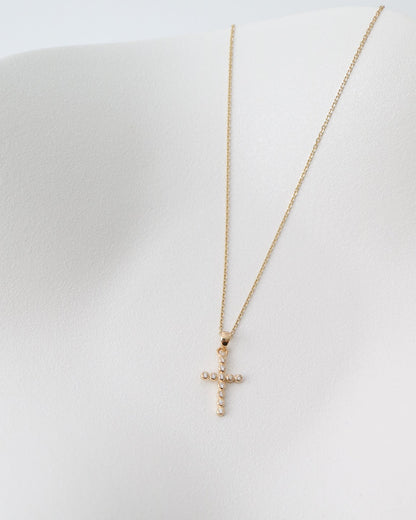 Gold necklace with a cross pendant on a white surface