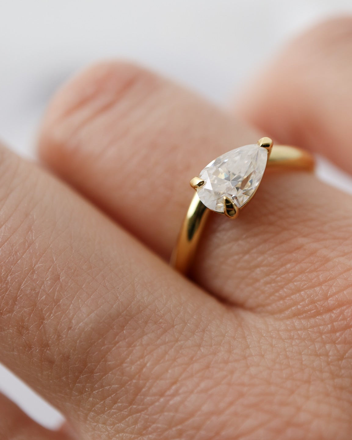 Gold ring with a pear-shaped diamond on a finger against a white background