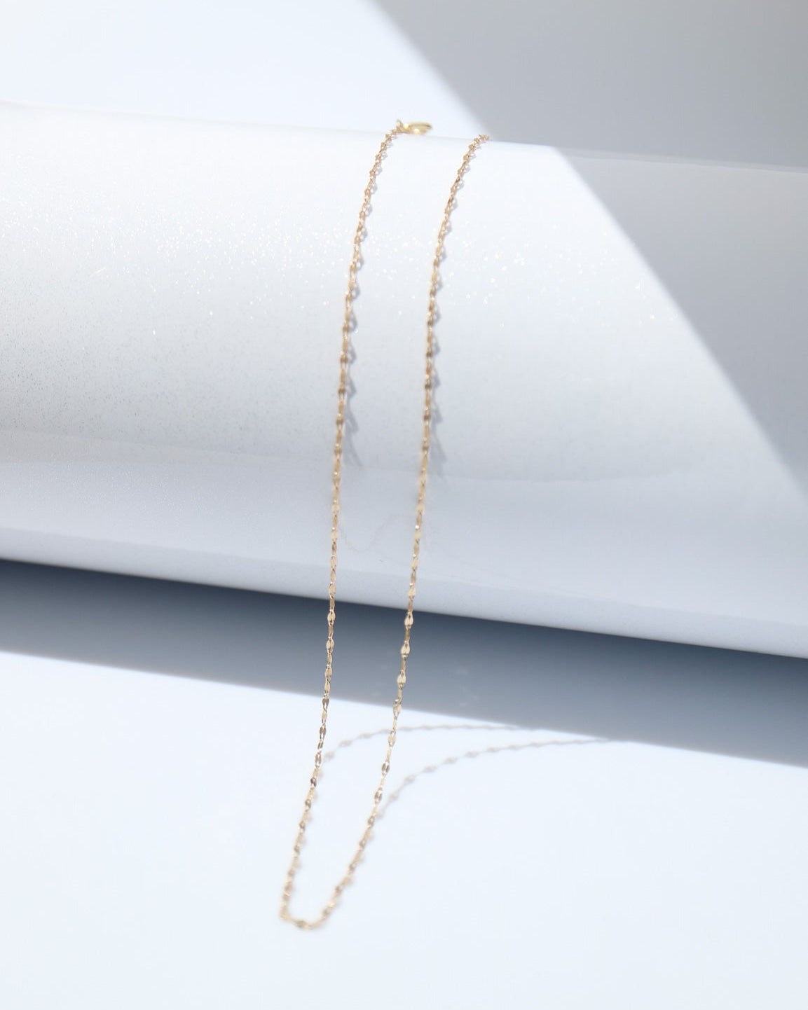 Gold necklace on a white surface with a gray geometric background