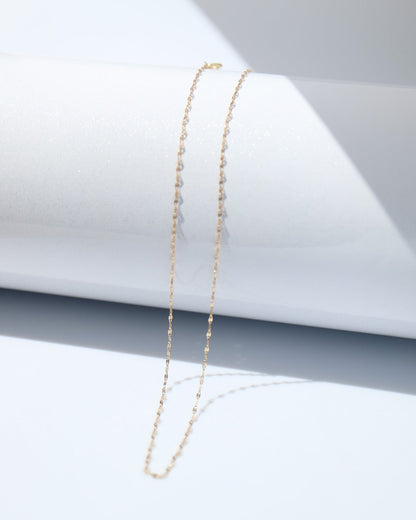 Gold necklace on a white surface with a gray geometric background