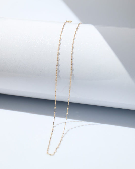 Gold necklace on a white surface with a gray geometric background