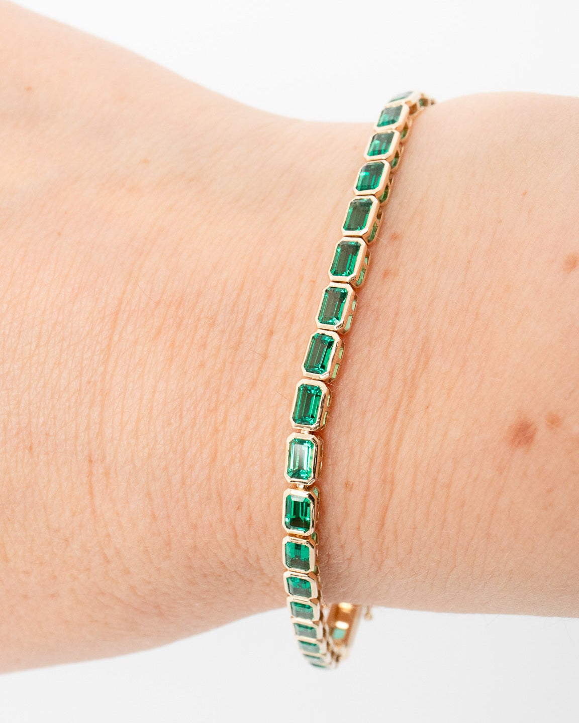 Gold bracelet with green gemstones on a wrist against a white background