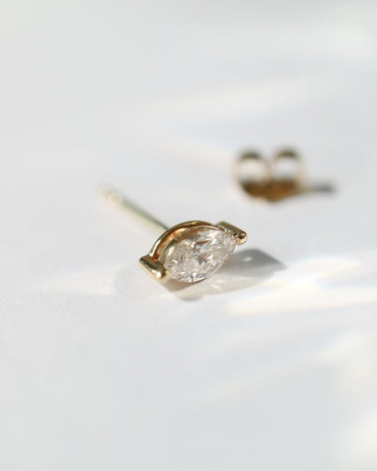 A pair of gold stud earrings with marquise-cut clear diamonds, photographed on a bright white surface with soft shadows.