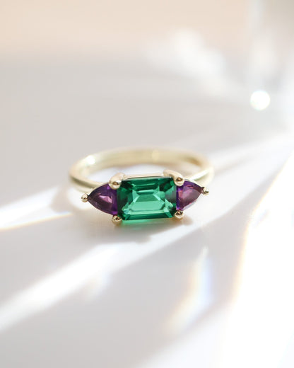 Gold ring with green and purple gemstones on a white background