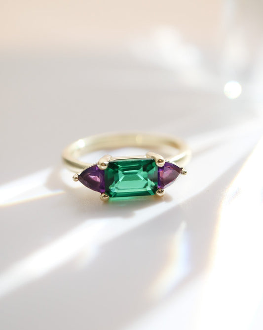 Gold ring with green and purple gemstones on a white background